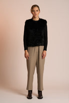 Woman wearing a black gilet over a black top with beige pants on a beige background