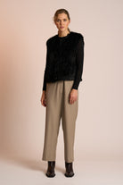 Woman wearing a black fur gilet over a black top with beige pants on a beige background
