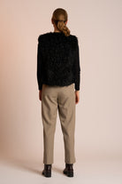 Woman wearing a black gilet over a black top with beige pants on a beige background back angle