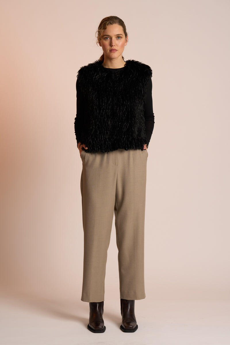 Woman wearing a black gilet over a black top with beige pants on a beige background