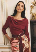 Woman wearing a burgundy top and patterned skirt in an elegant interior setting.