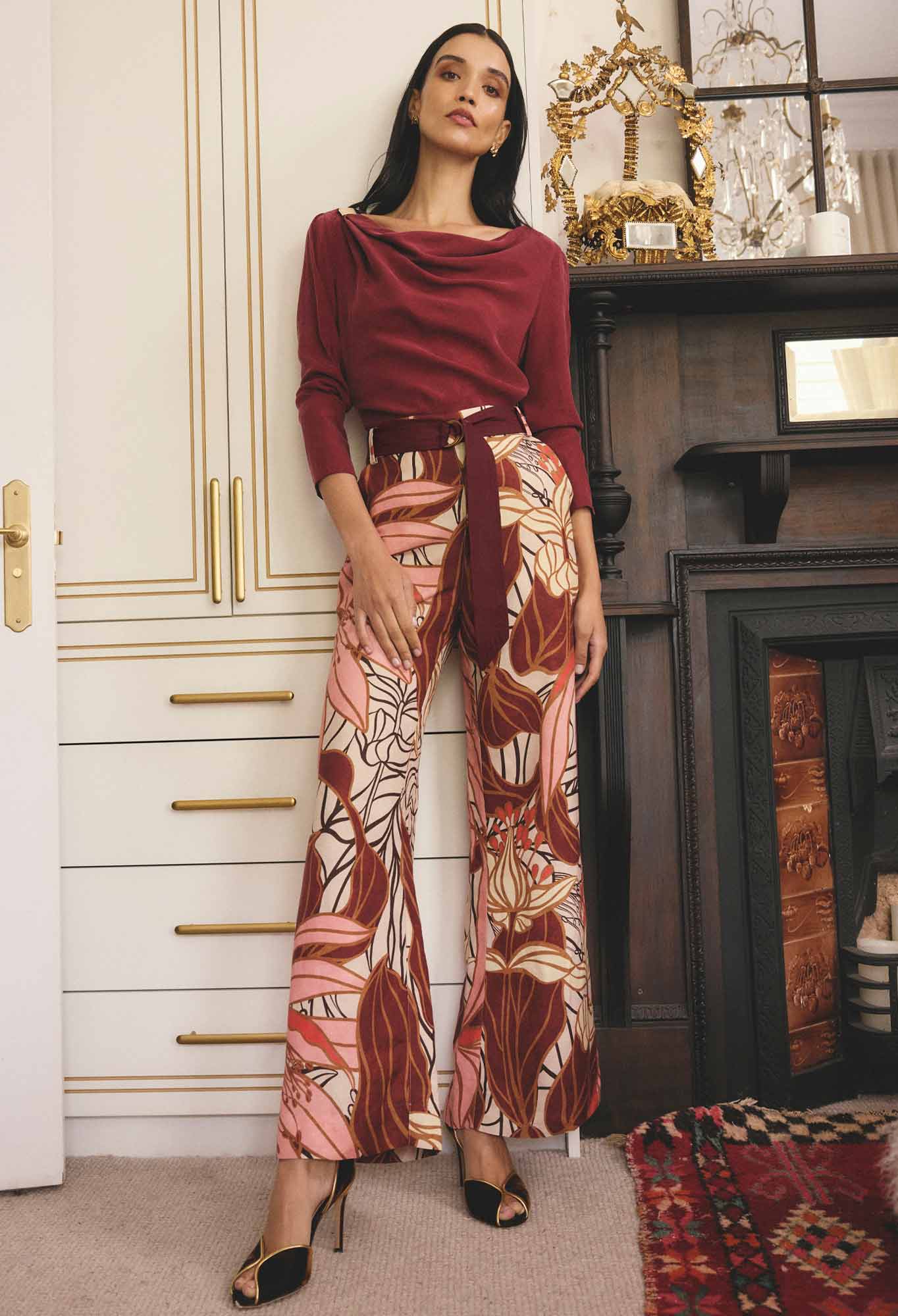 Woman wearing a burgundy top and patterned pants in a room with decorative elements.