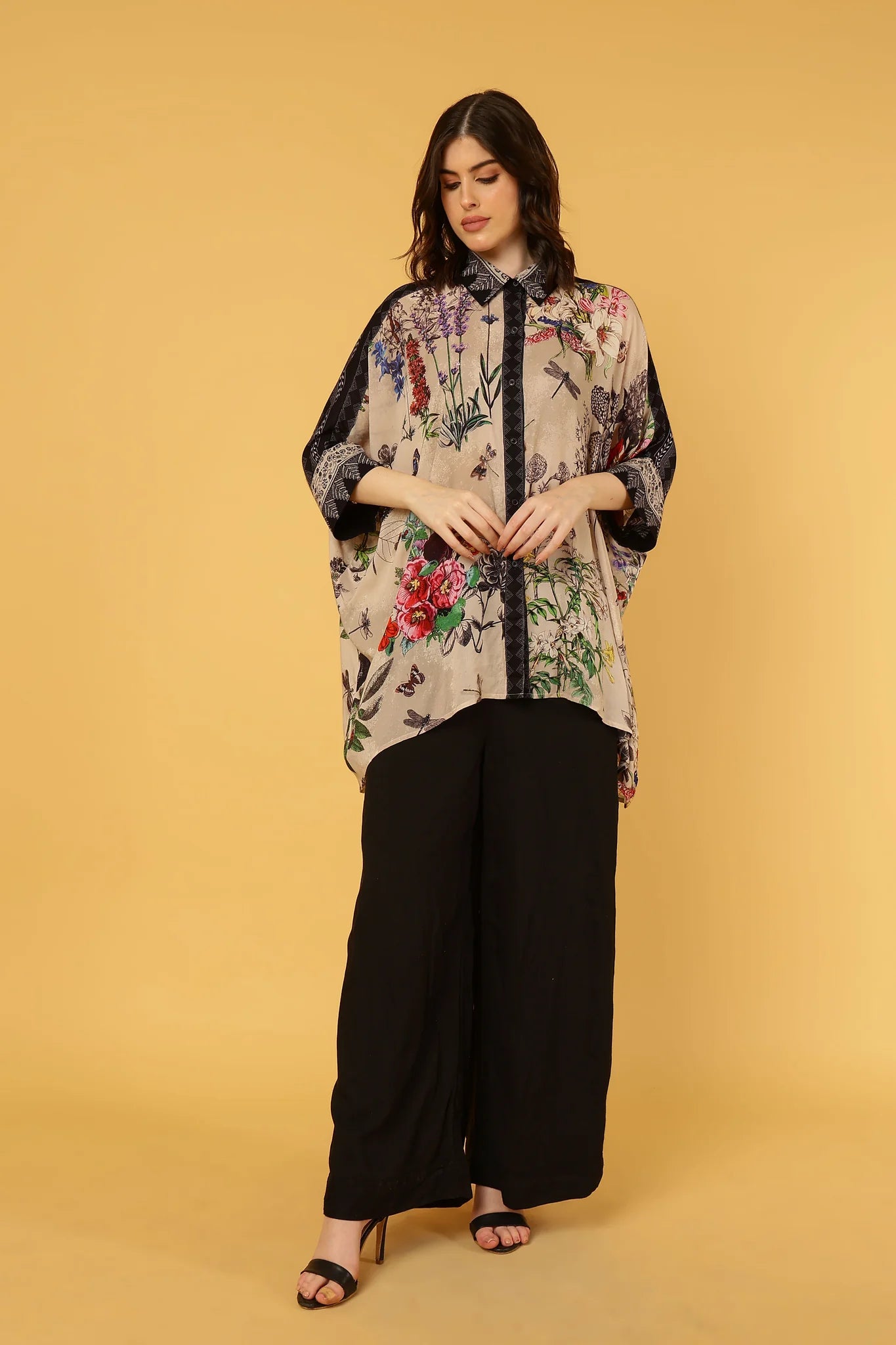 Woman wearing a floral kimono-style shirt and black pants on a beige background