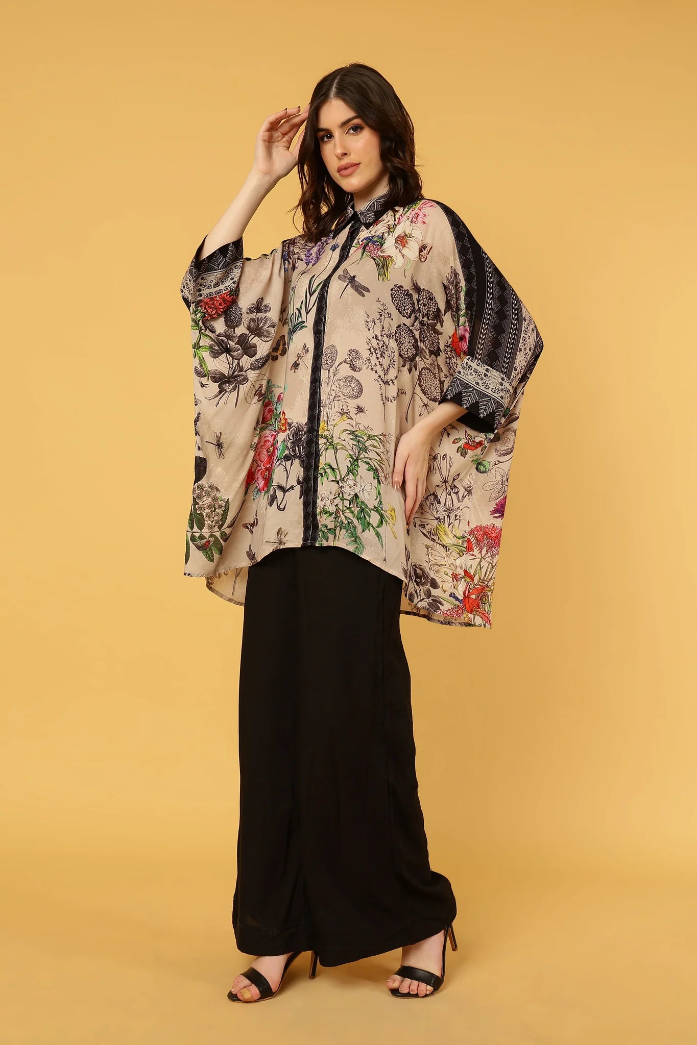 Woman wearing a floral kimono over a black outfit on a beige background