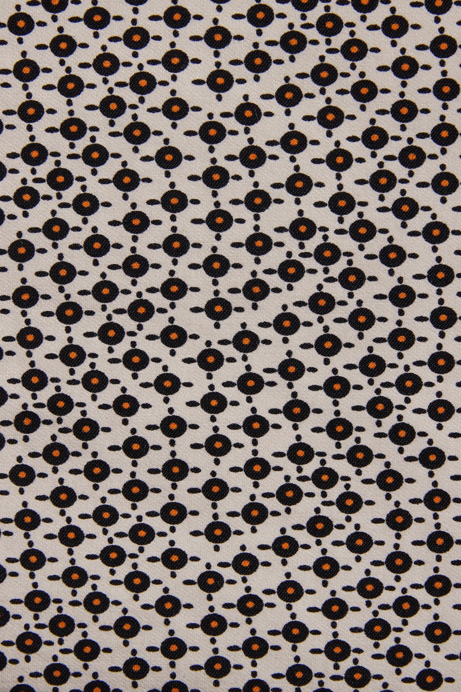A close-up of a fabric pattern featuring a repeating geometric design of small black circles and dots on a light beige background, with some motifs highlighted in orange.