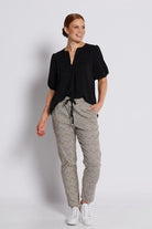 A woman modeling a black short-sleeve blouse with a split neckline and patterned drawstring trousers featuring a black and beige geometric print, paired with white sneakers, against a light gray studio background.