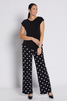 A woman modeling a black short-sleeve top and black wide-leg pants with white polka dots, standing against a light gray studio background.