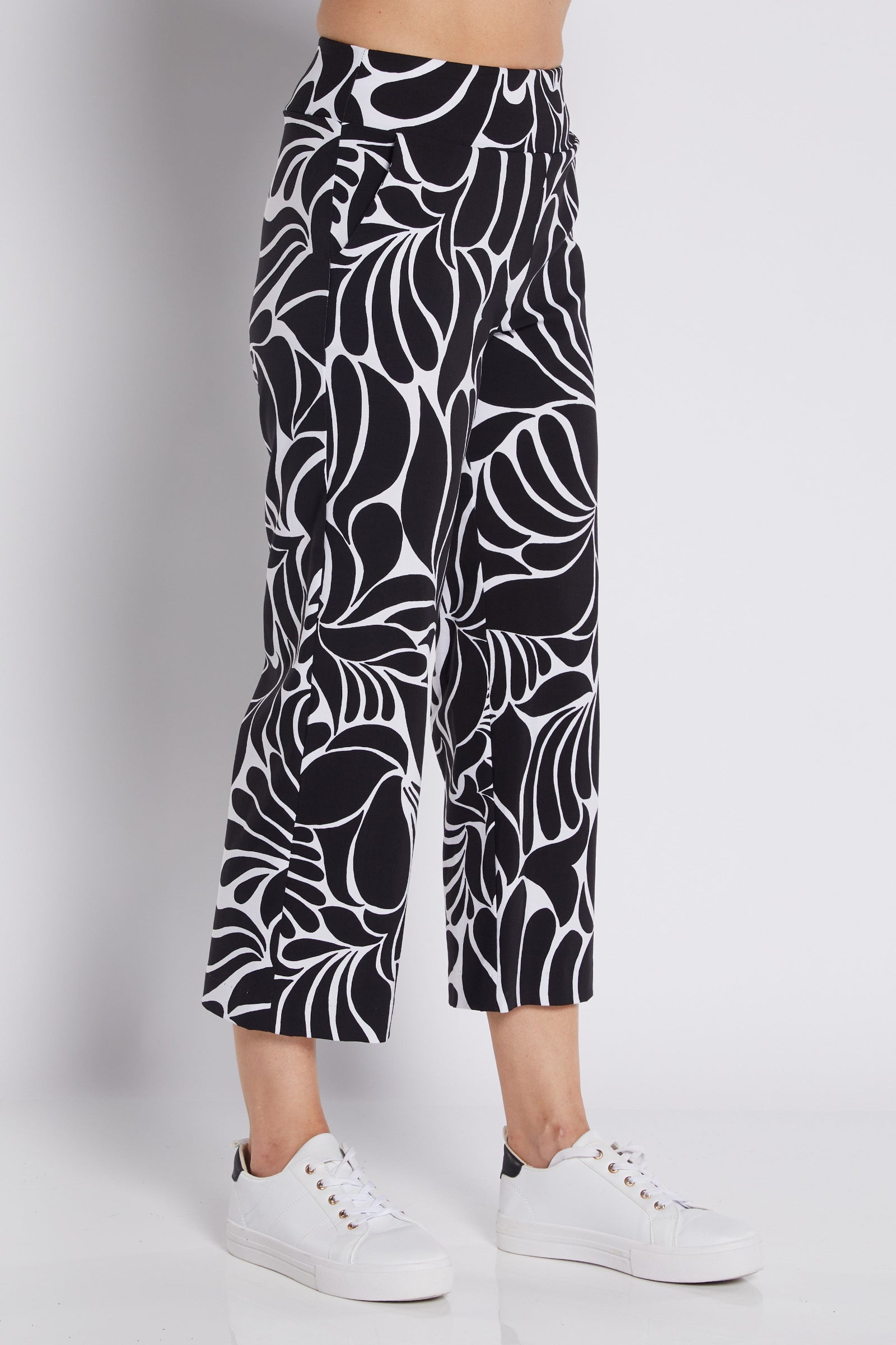 Black and white abstract patterned cropped pants worn by a model with white sneakers, photographed against a light gray studio background.