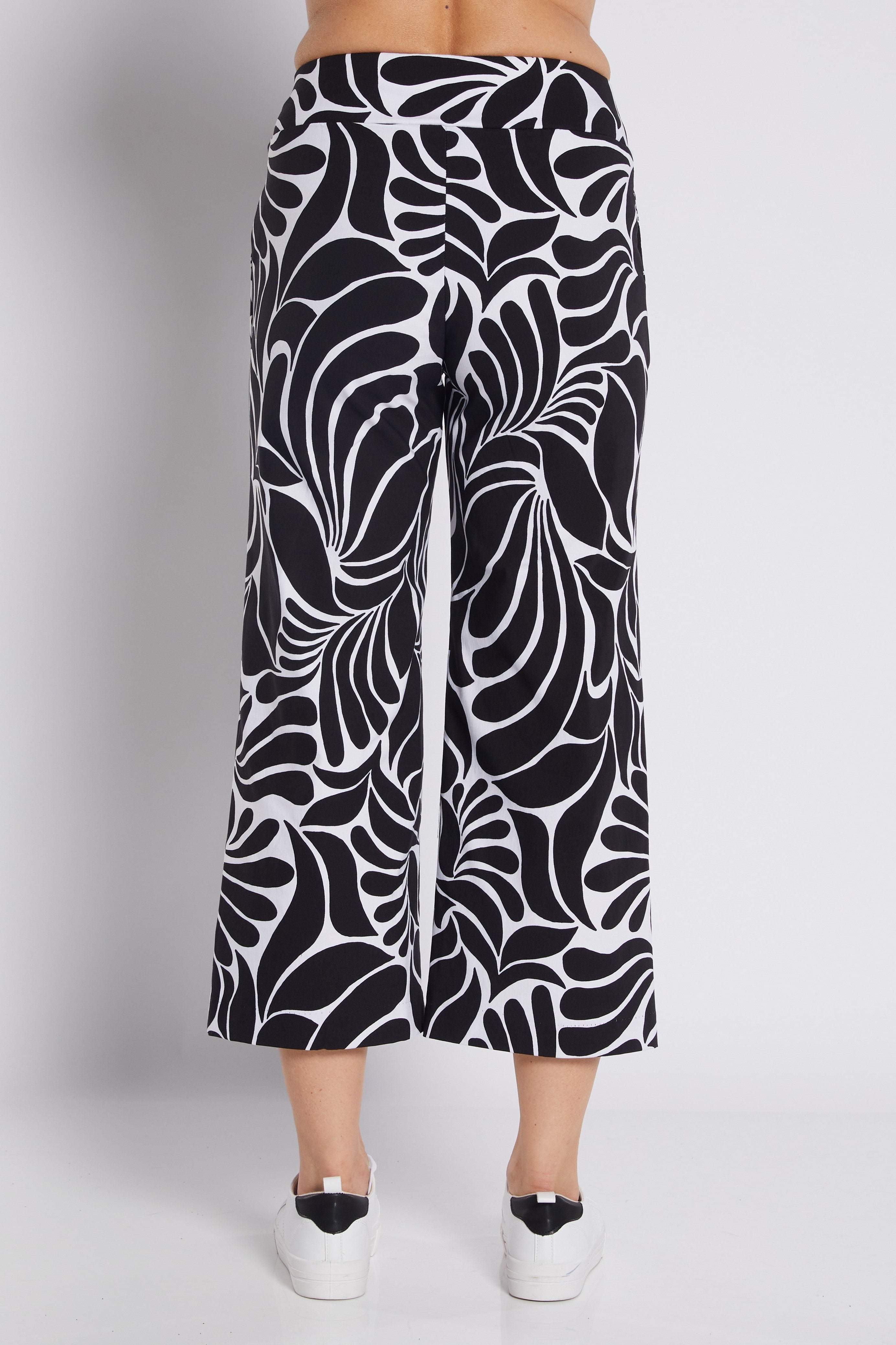Black and white abstract patterned cropped pants shown on a model from the back, paired with white platform sneakers against a light gray studio background.