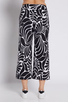 Black and white abstract patterned cropped pants shown on a model from the back, paired with white platform sneakers against a light gray studio background.