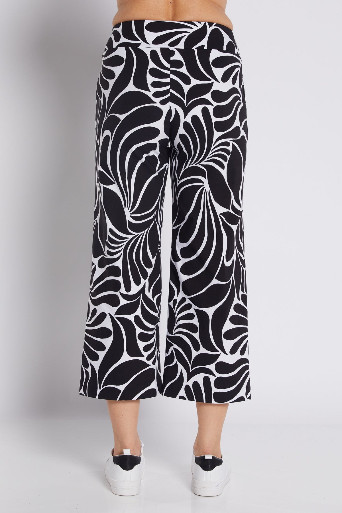 Black and white abstract patterned cropped pants shown on a model from the back, paired with white platform sneakers against a light gray studio background.