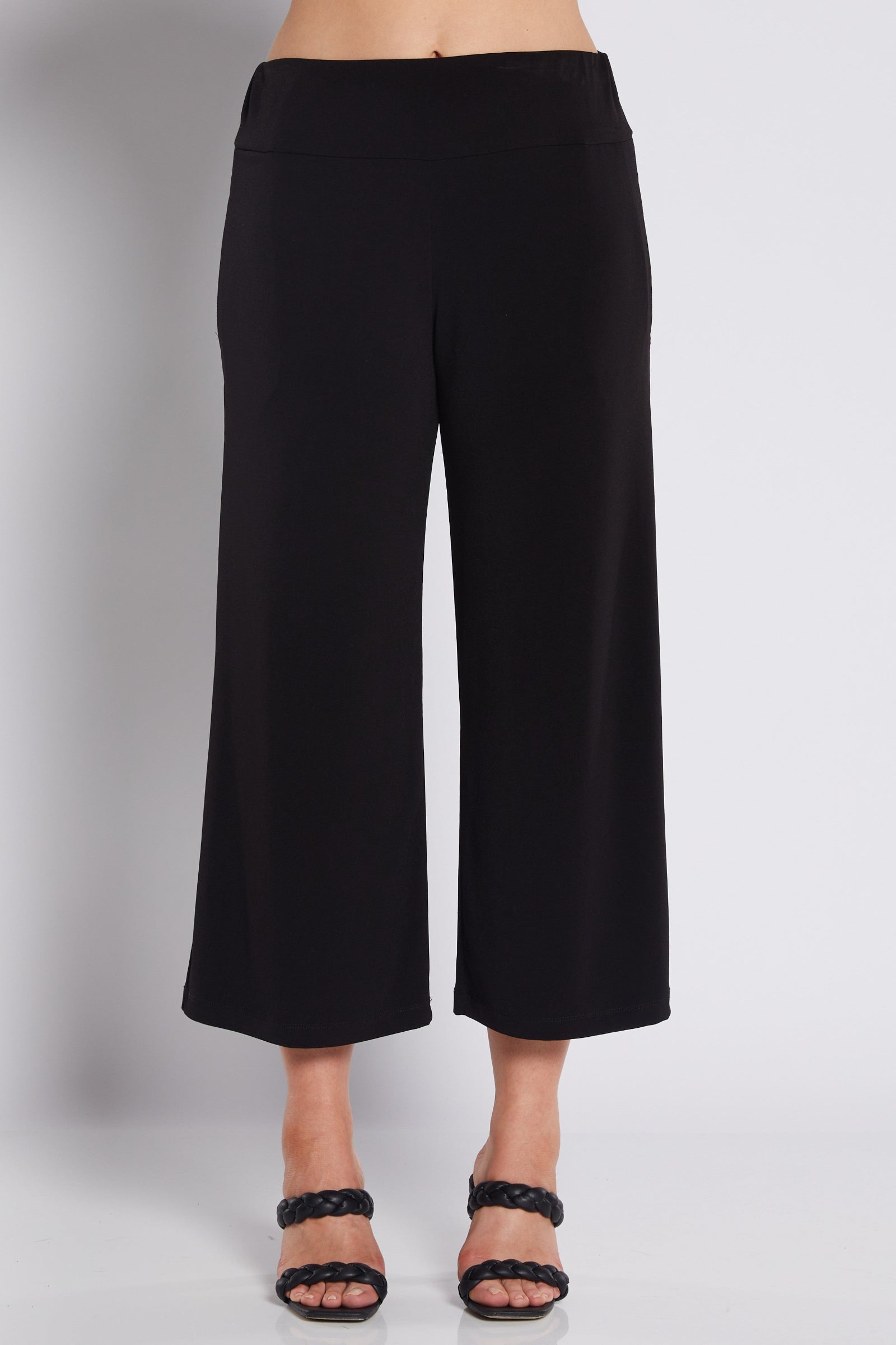 Black cropped wide-leg pants shown on a model from the waist down, paired with black strappy heeled sandals against a light gray studio background.