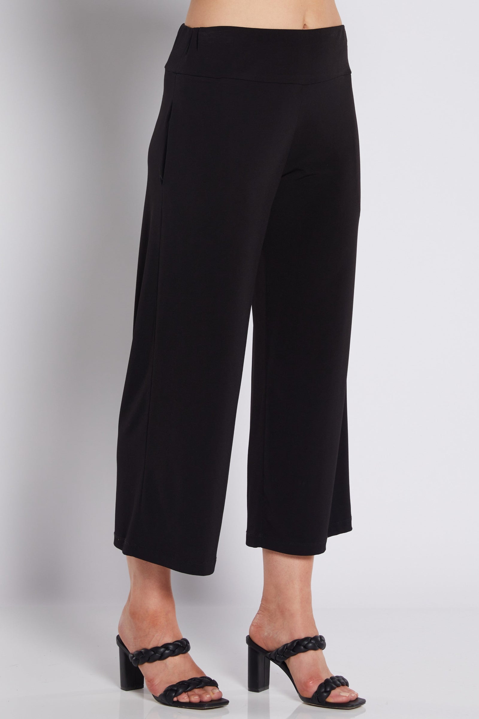 Black cropped wide-leg pants shown on a model from the waist down, paired with black heeled sandals against a light gray studio background.