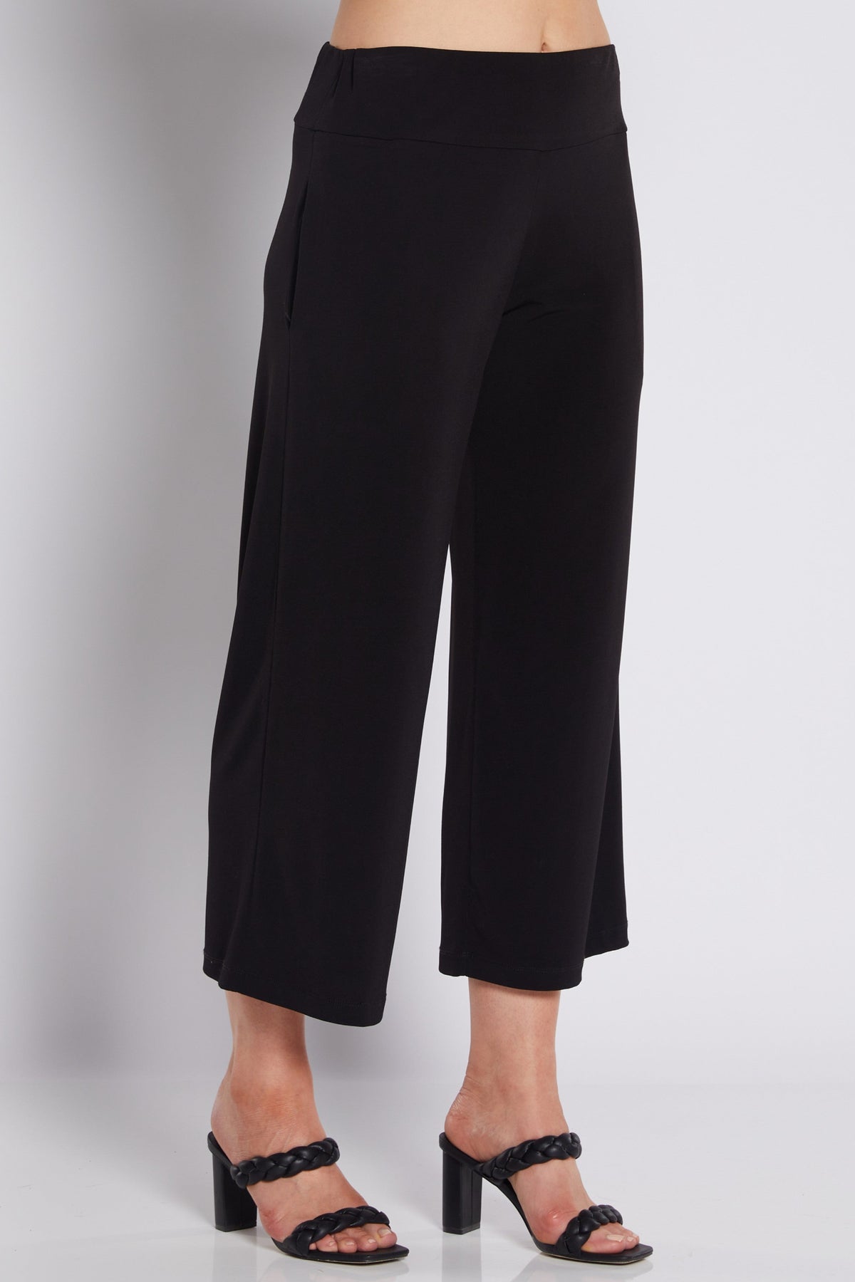 Black cropped wide-leg pants shown on a model from the waist down, paired with black heeled sandals against a light gray studio background.