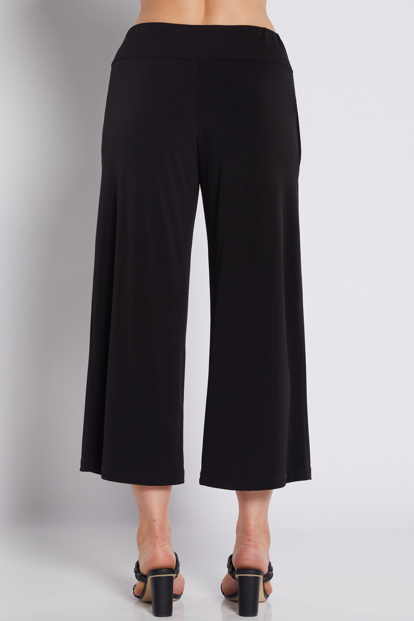 Black wide-leg cropped pants shown from the back on a model, paired with black block-heel sandals against a light gray studio background.