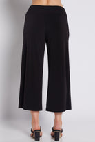 Black wide-leg cropped pants shown from the back on a model, paired with black block-heel sandals against a light gray studio background.