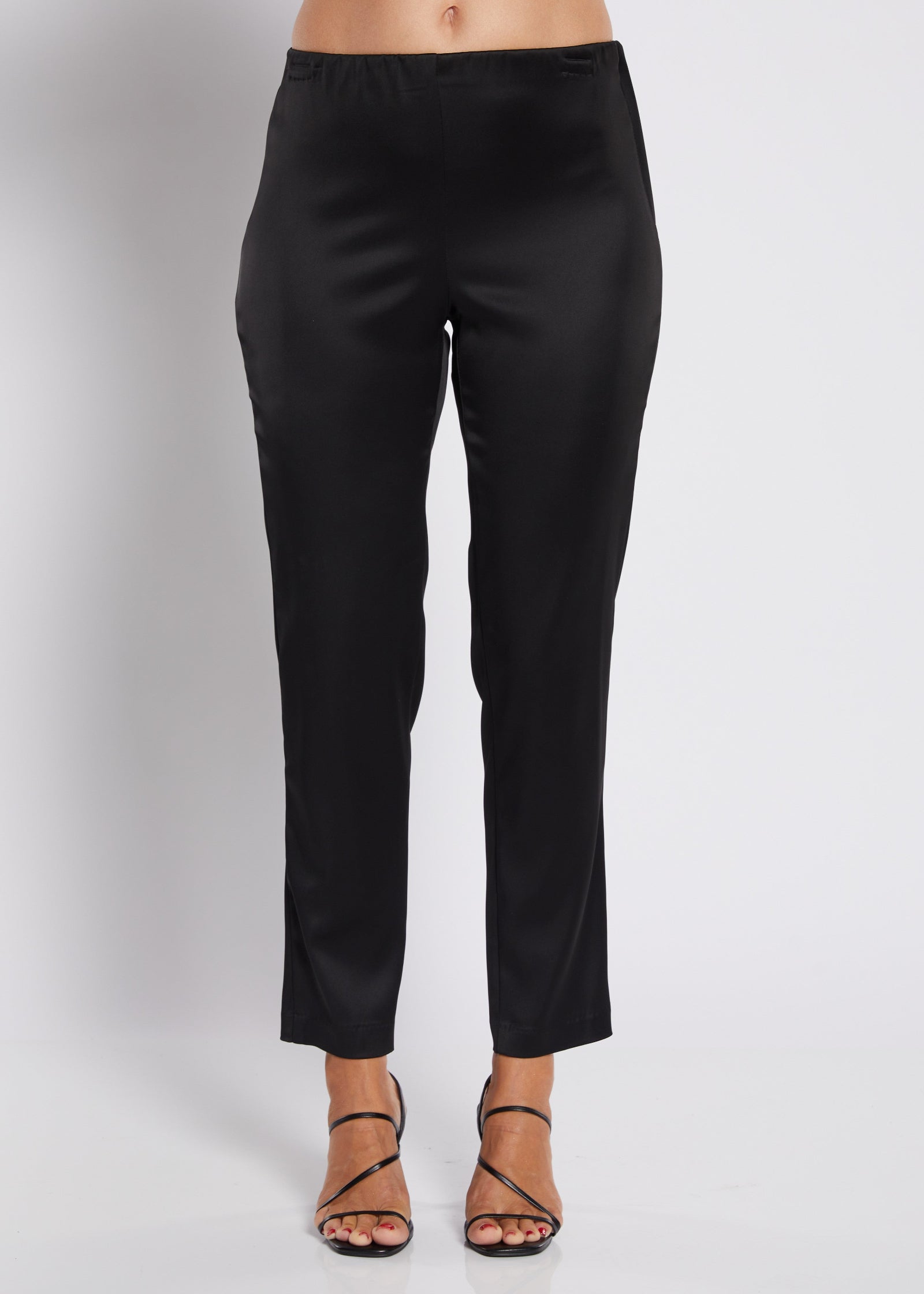 Black cropped pants shown on a model from the waist down, paired with black strappy high-heeled sandals against a light gray studio background.