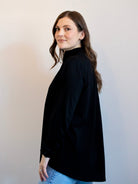 Woman wearing a black turtleneck and blue jeans against a plain background