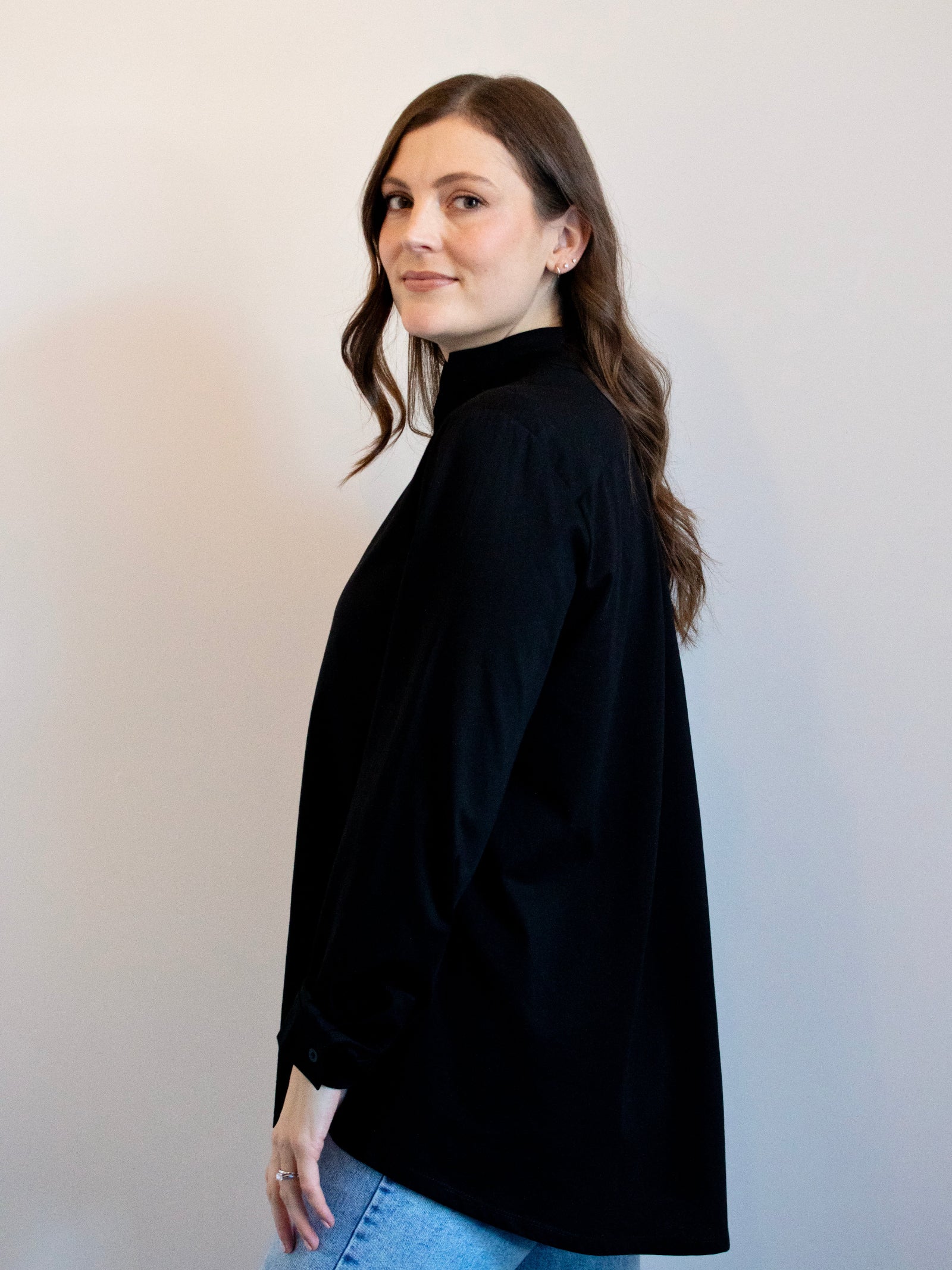 Woman wearing a black turtleneck and blue jeans against a plain background