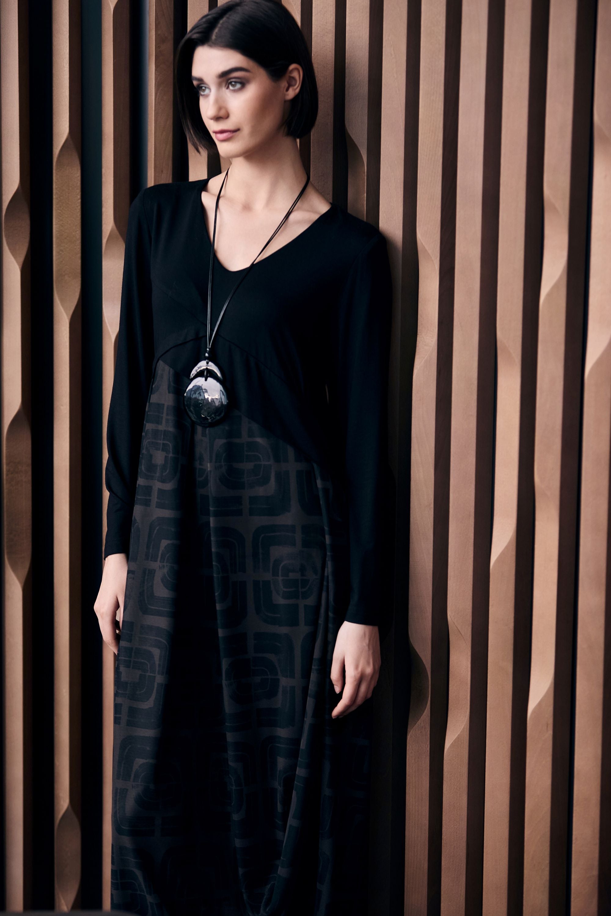 Woman wearing a black and brown patterned dress standing against a textured wall.