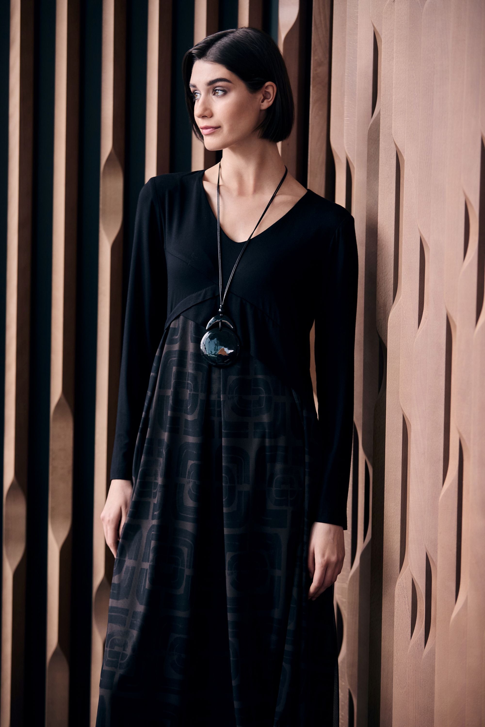 Woman wearing a black and brown patterned dress standing against a textured wall.