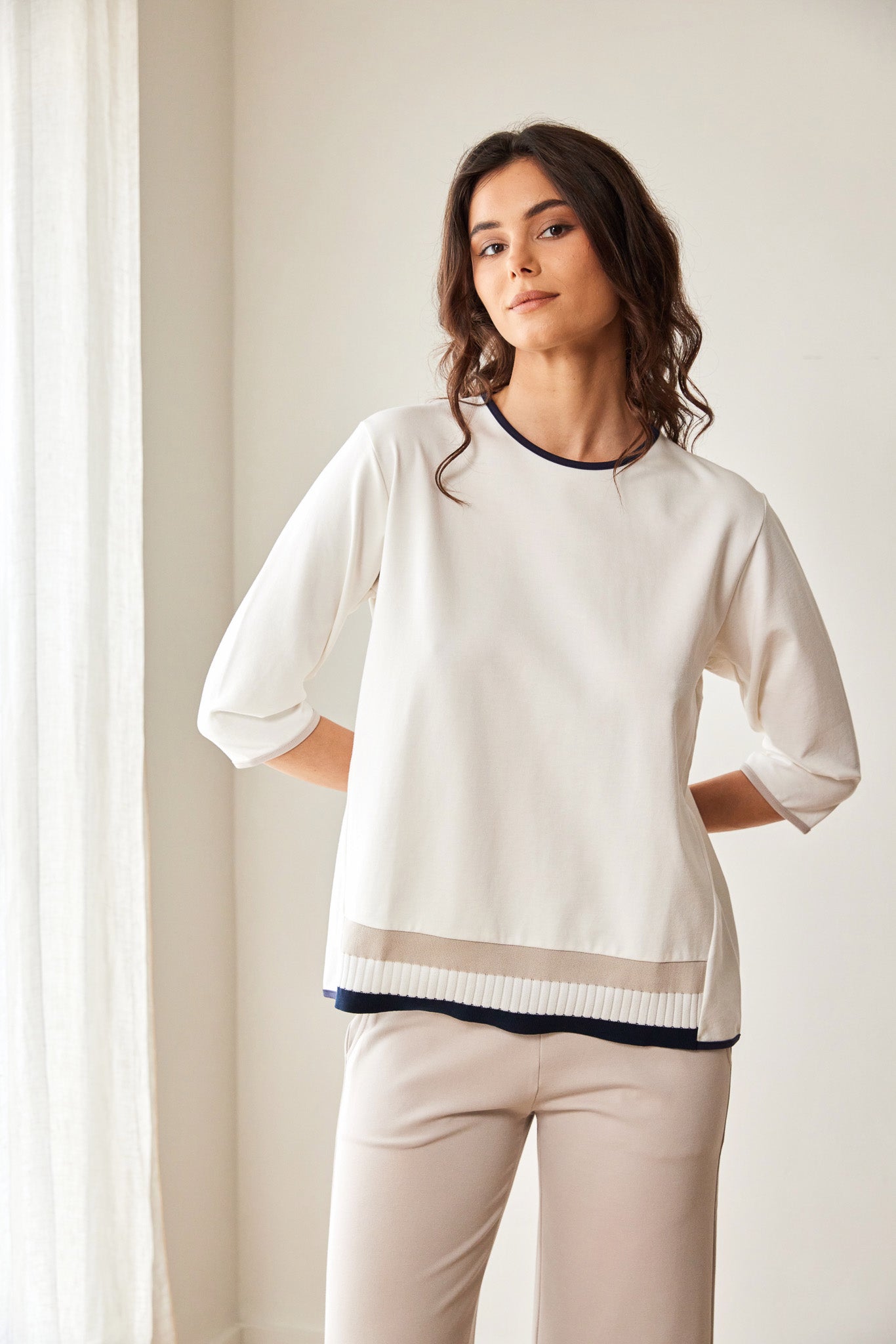 Woman wearing a white sweater with a subtle pattern and beige pants against a neutral background