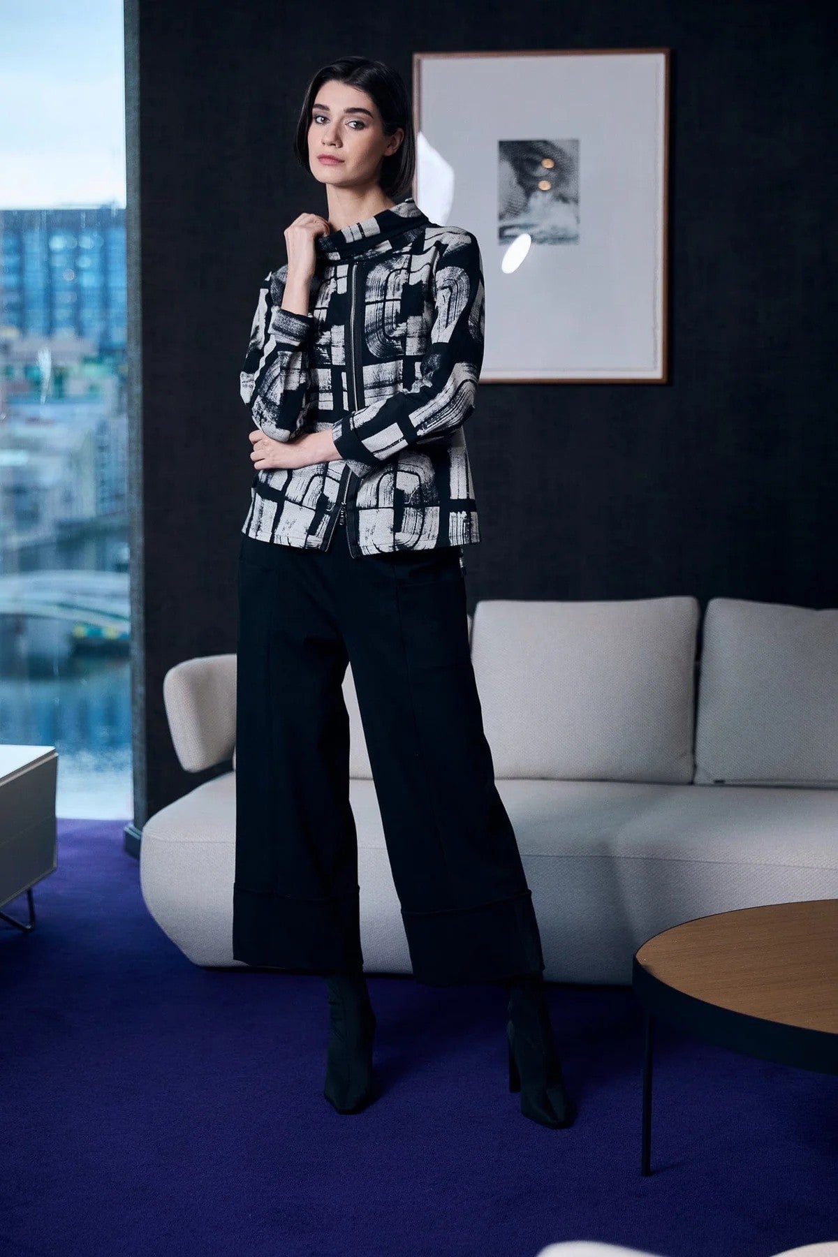 Woman in a black and white jacket and black wide pants standing in a modern room 