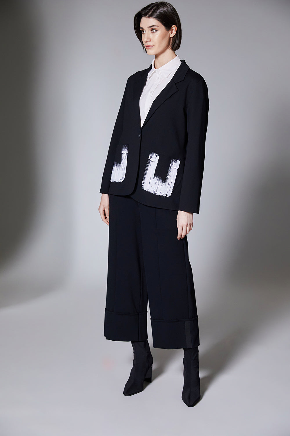 Person wearing a black jacket with black wide cuff pants on a gray background