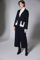 Person wearing a black jacket with black wide cuff pants on a gray background