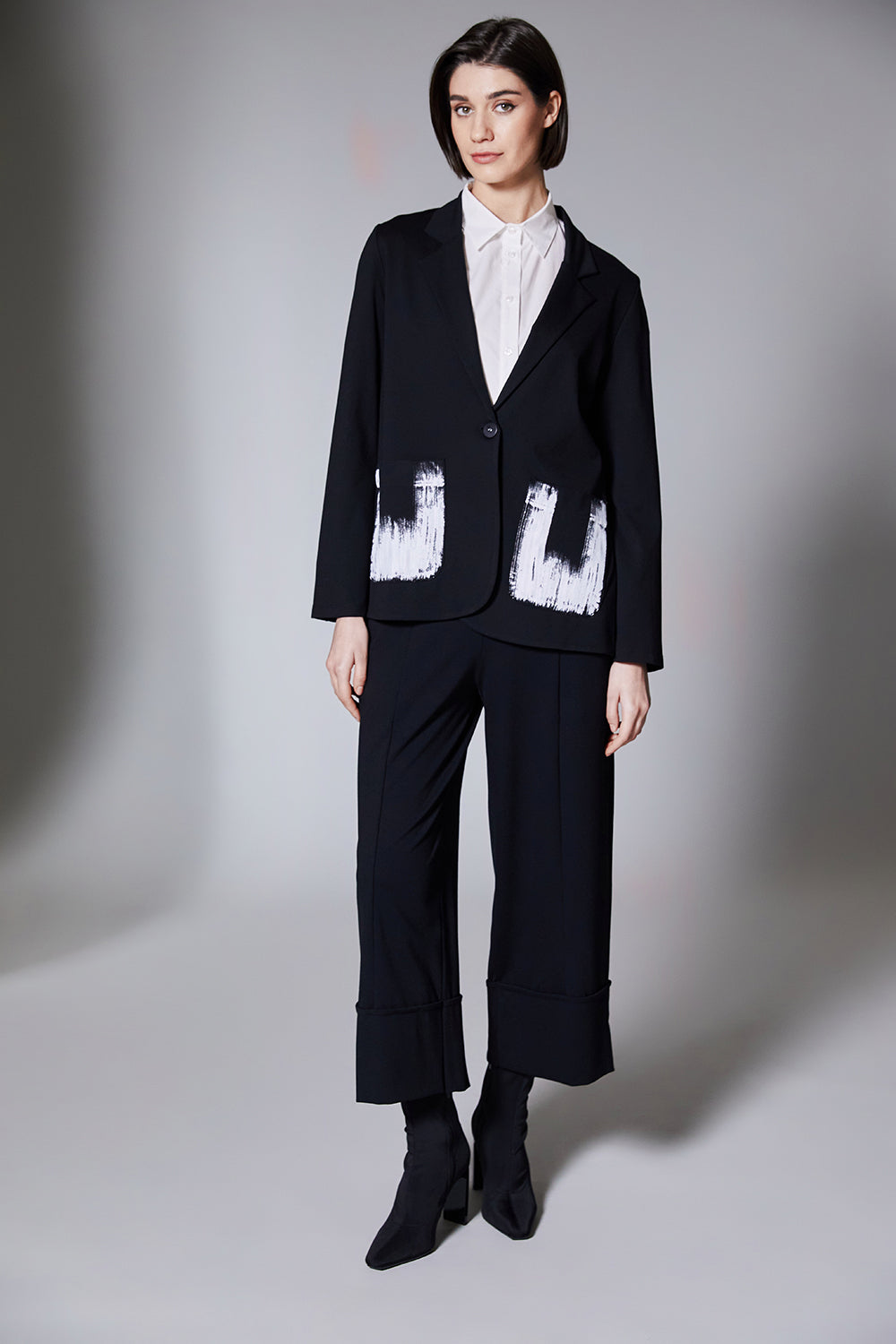 Person wearing a black jacket with black wide cuff pants on a gray background