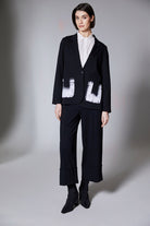 Person wearing a black jacket with black wide cuff pants on a gray background