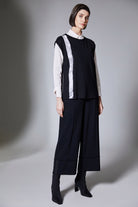 Woman wearing a black sleeveless top with white trim and wide-leg pants on a gray background