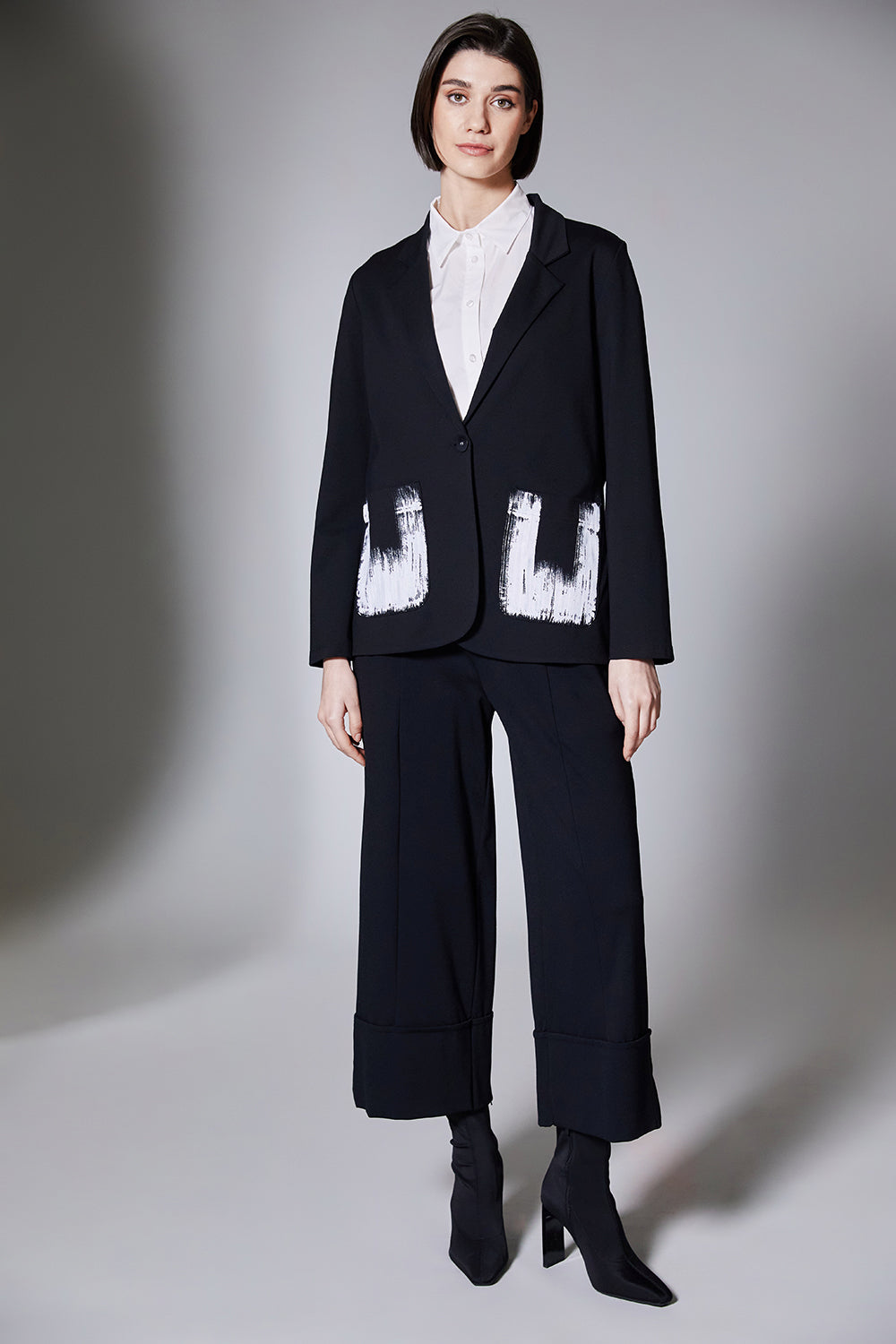 Person wearing a black jacket with black wide cuff pants on a gray background