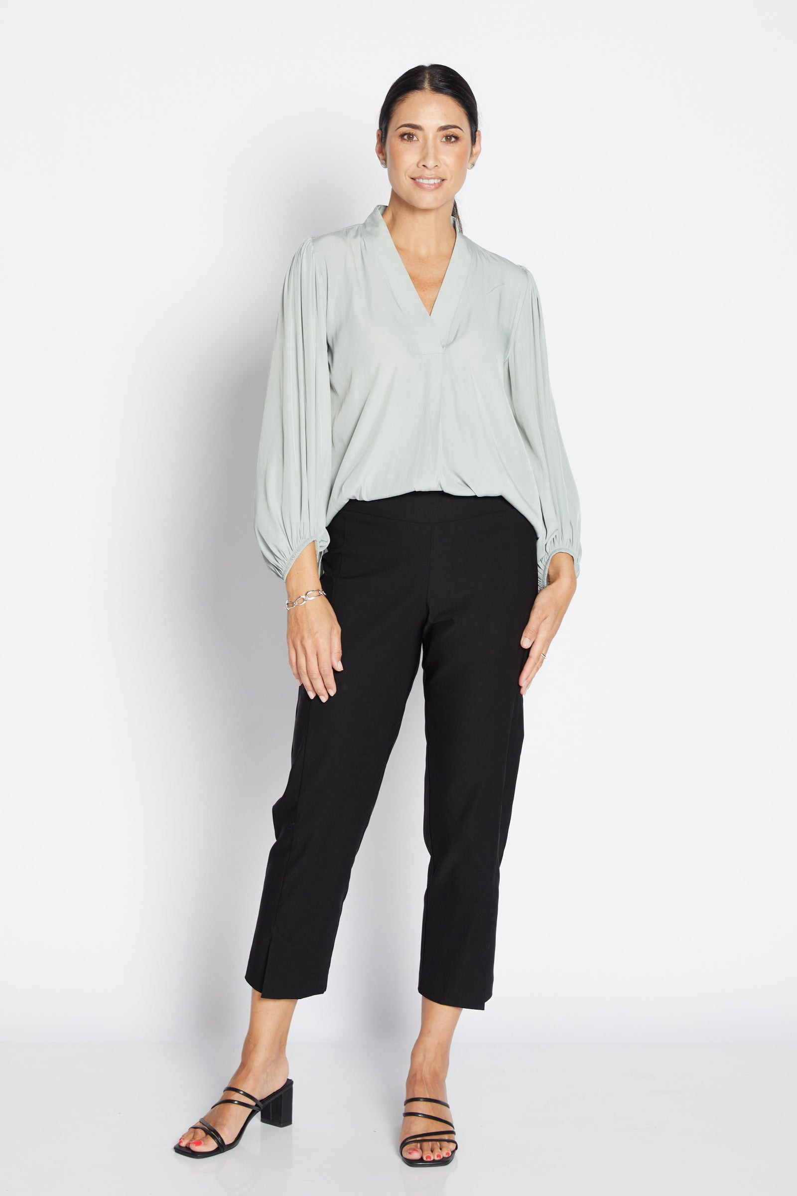 Woman wearing a light green blouse and black pants on a white background