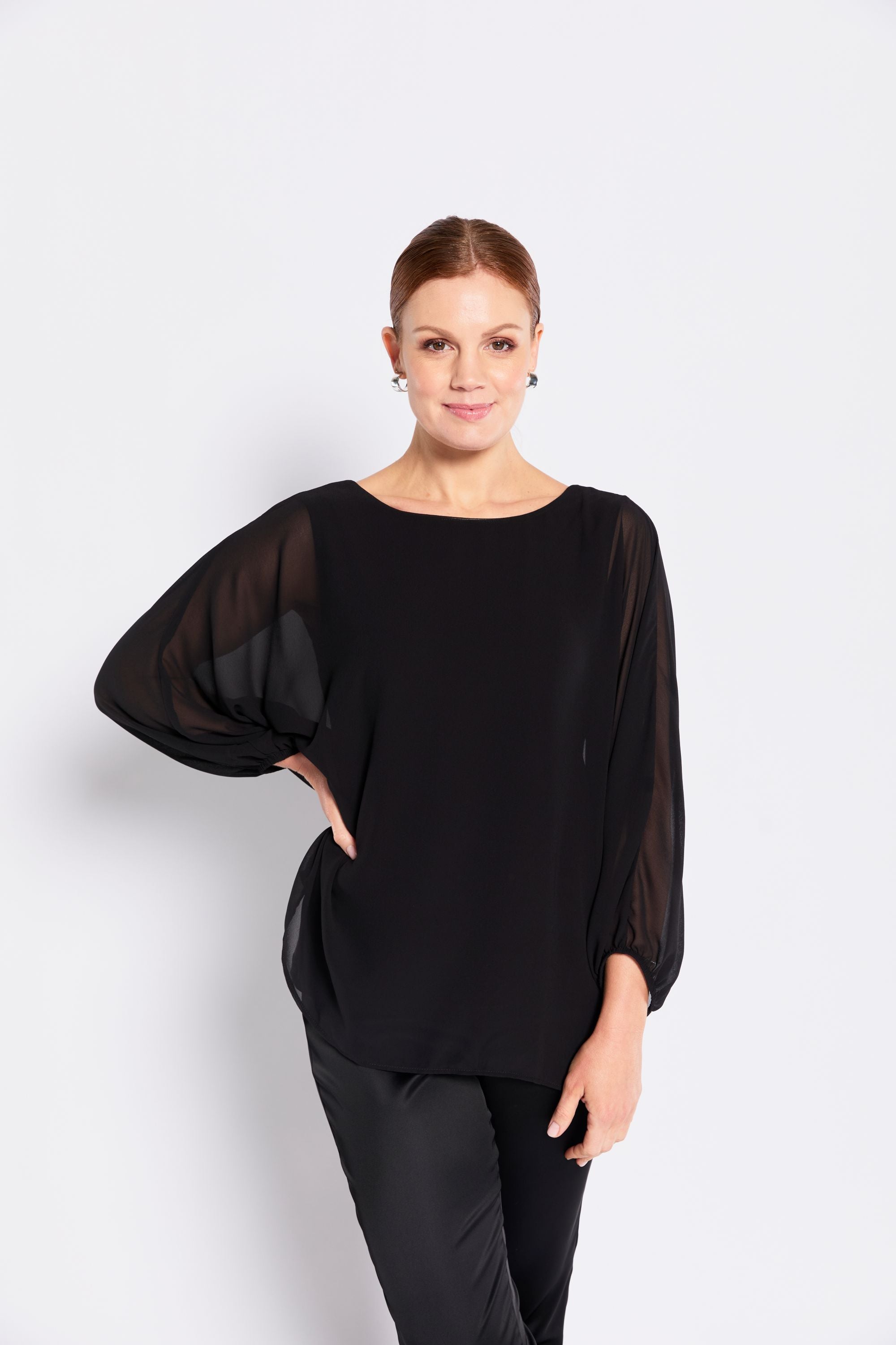 Woman wearing a black blouse with sheer sleeves on a white background