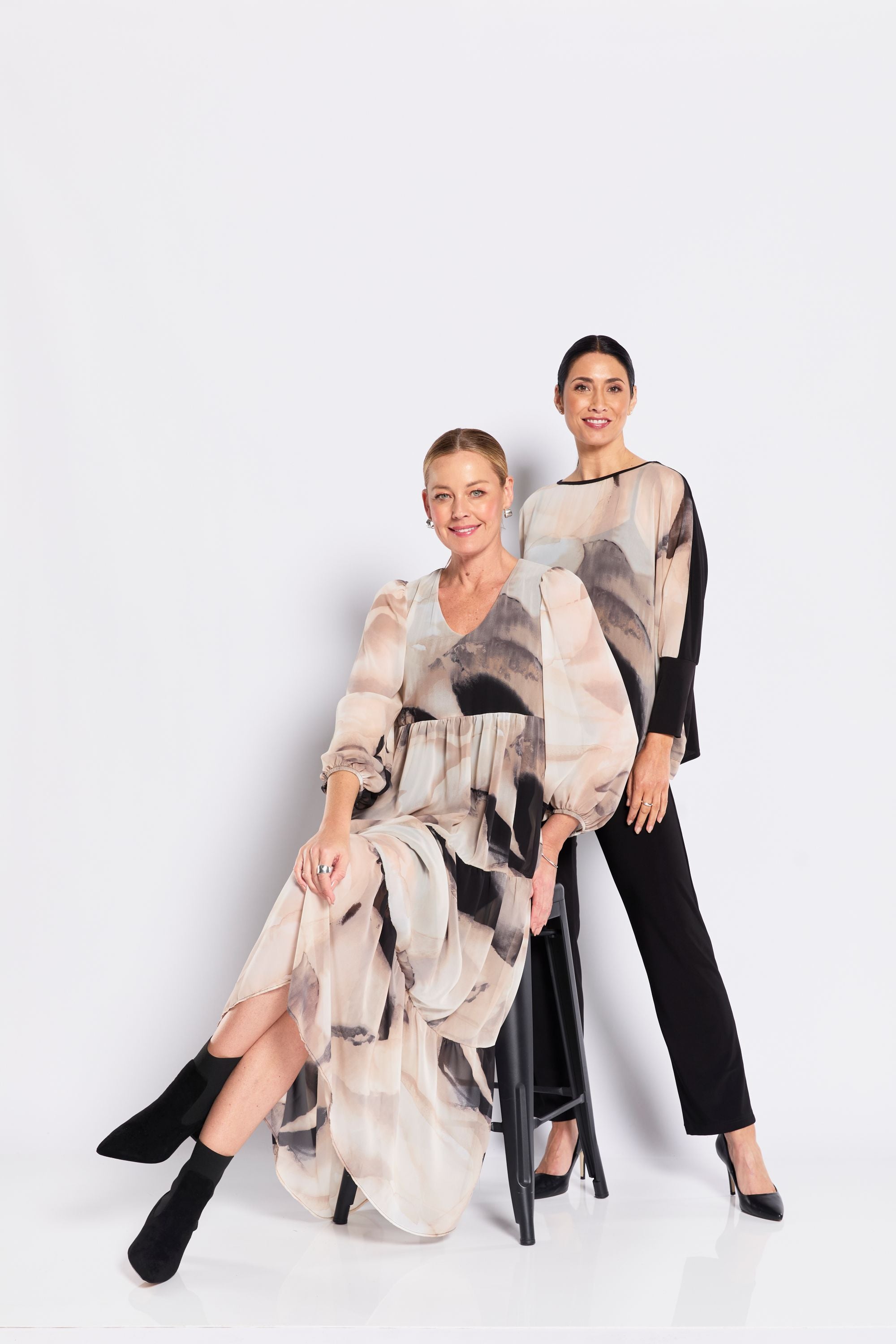 Two women wearing abstract print dress and top on a white background