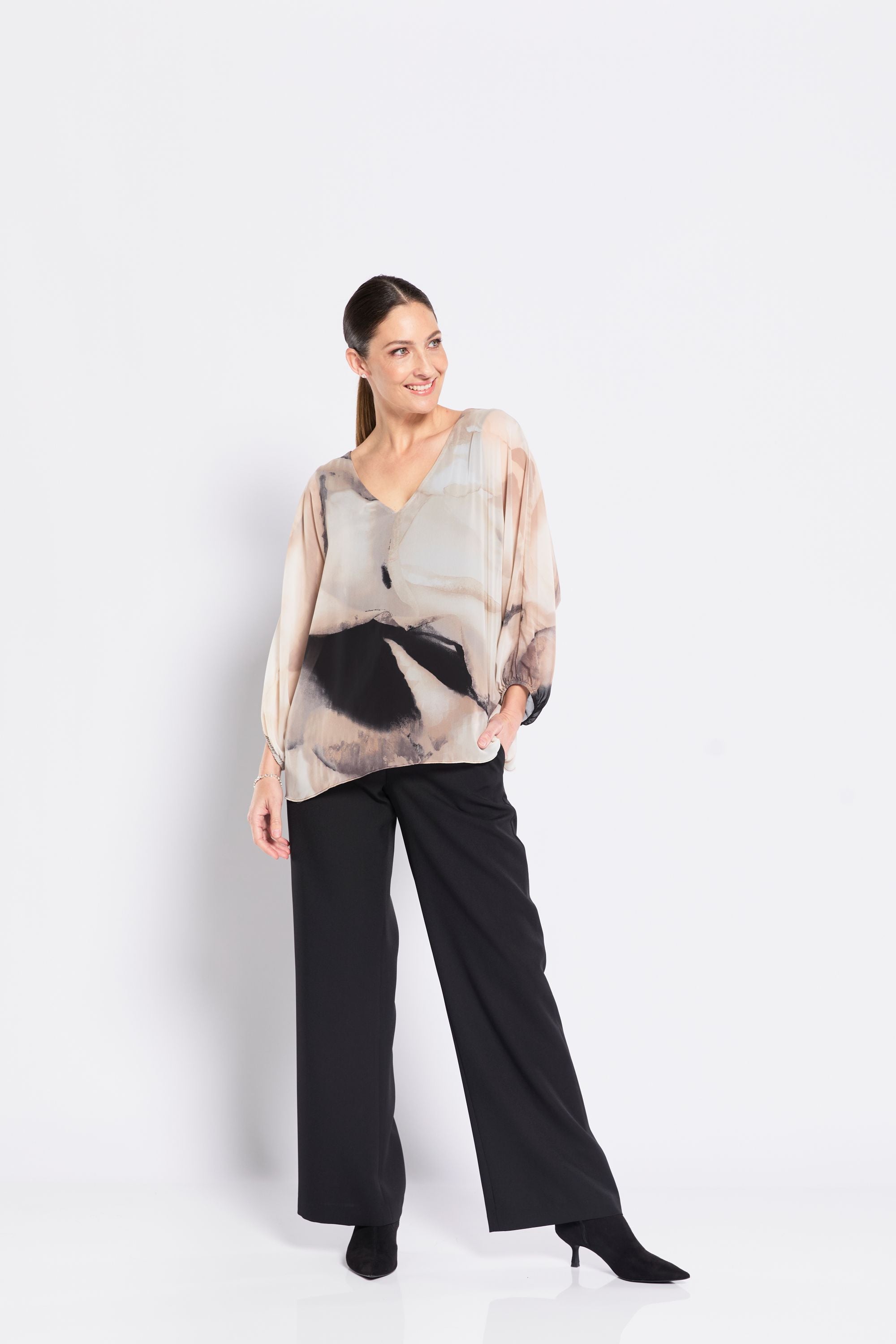 Woman wearing a patterned blouse and black pants on a white background