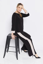 Woman sitting on a black stool wearing a black outfit with white stripes.