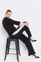 Woman sitting on a black stool wearing a black outfit with white stripes against a white background