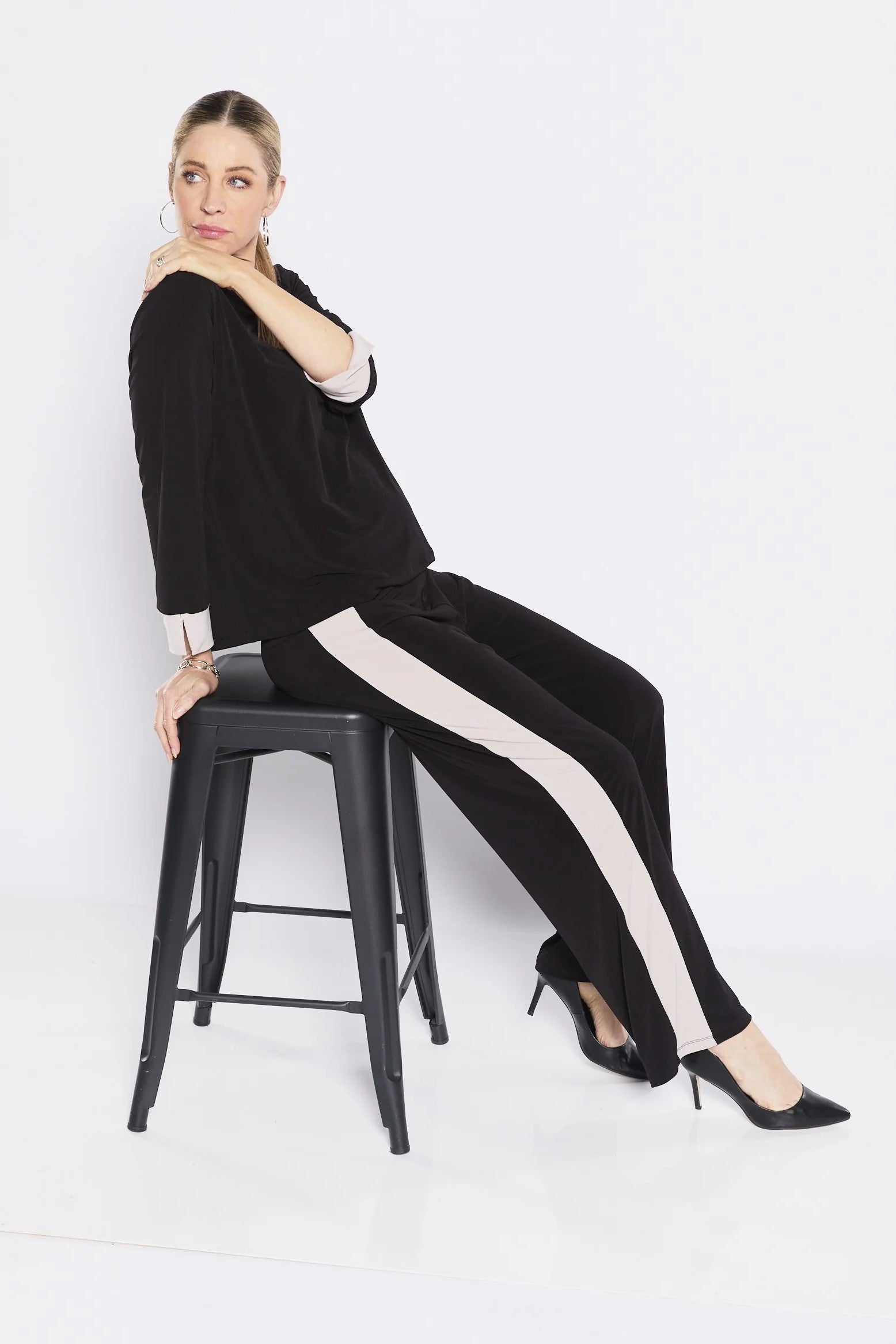 Woman sitting on a black stool wearing a black outfit with white stripes.