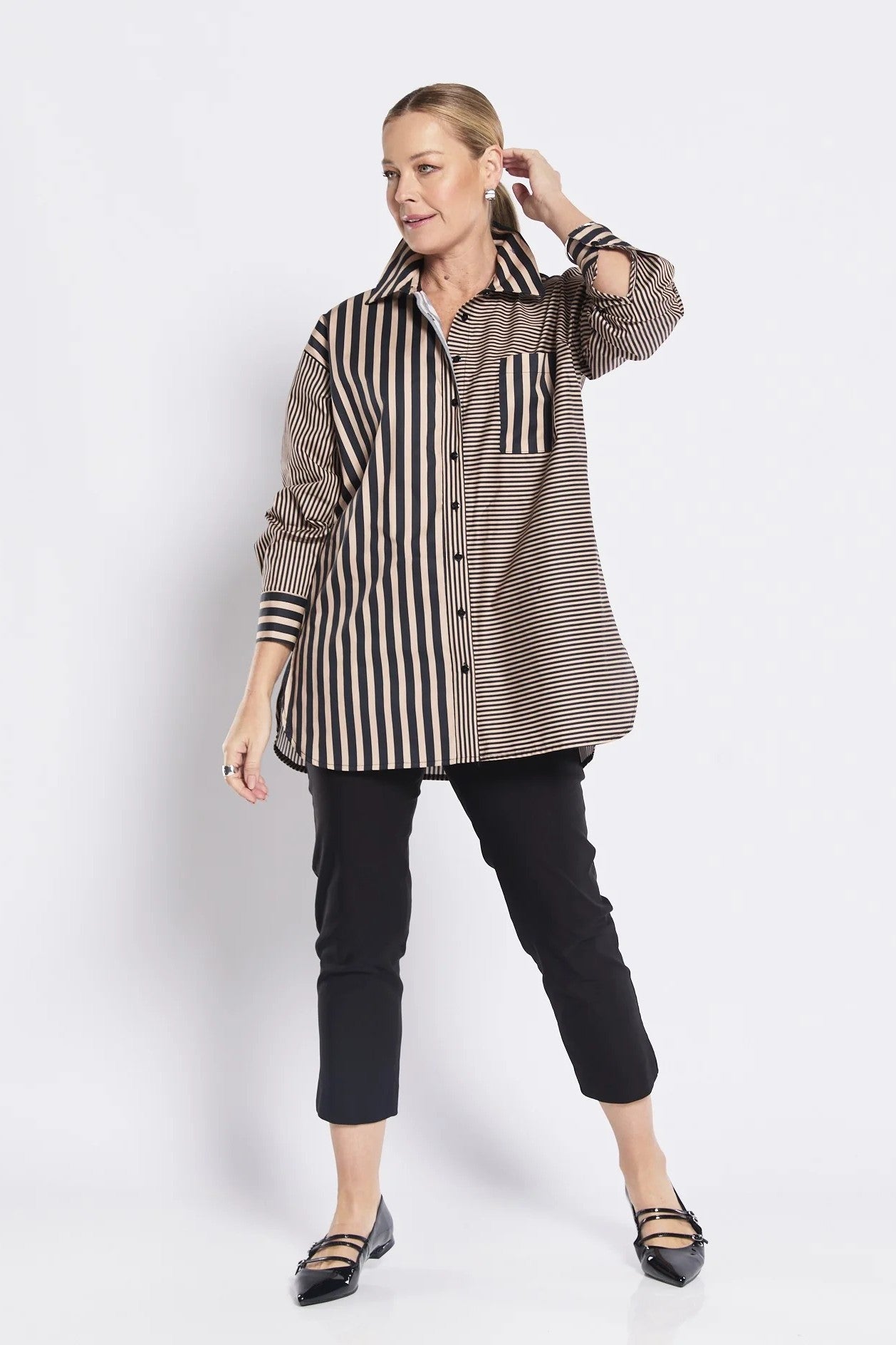 Woman wearing a long, patterned shirt with black pants on a white background