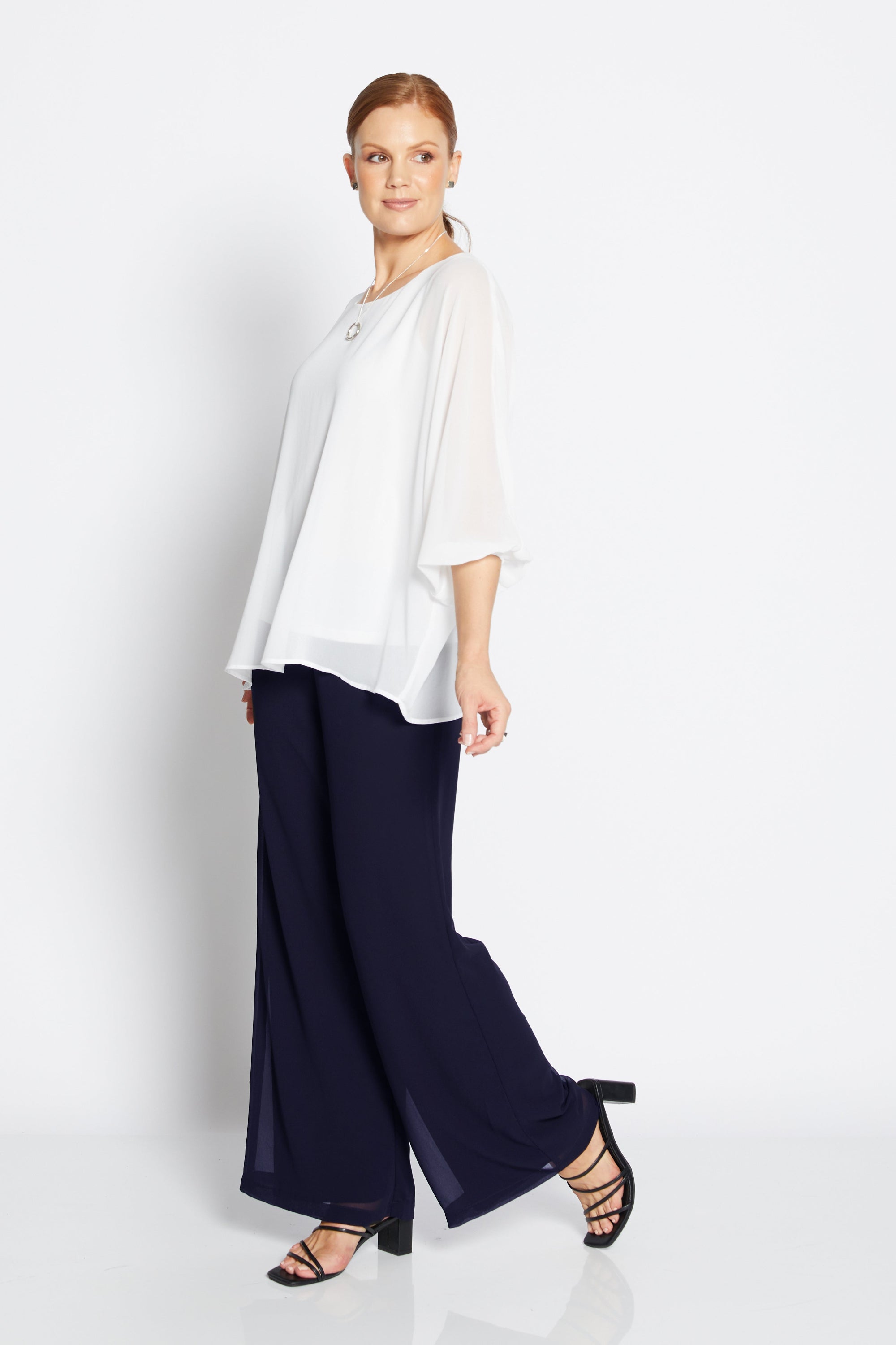 Woman wearing a white blouse and navy pants on a white background