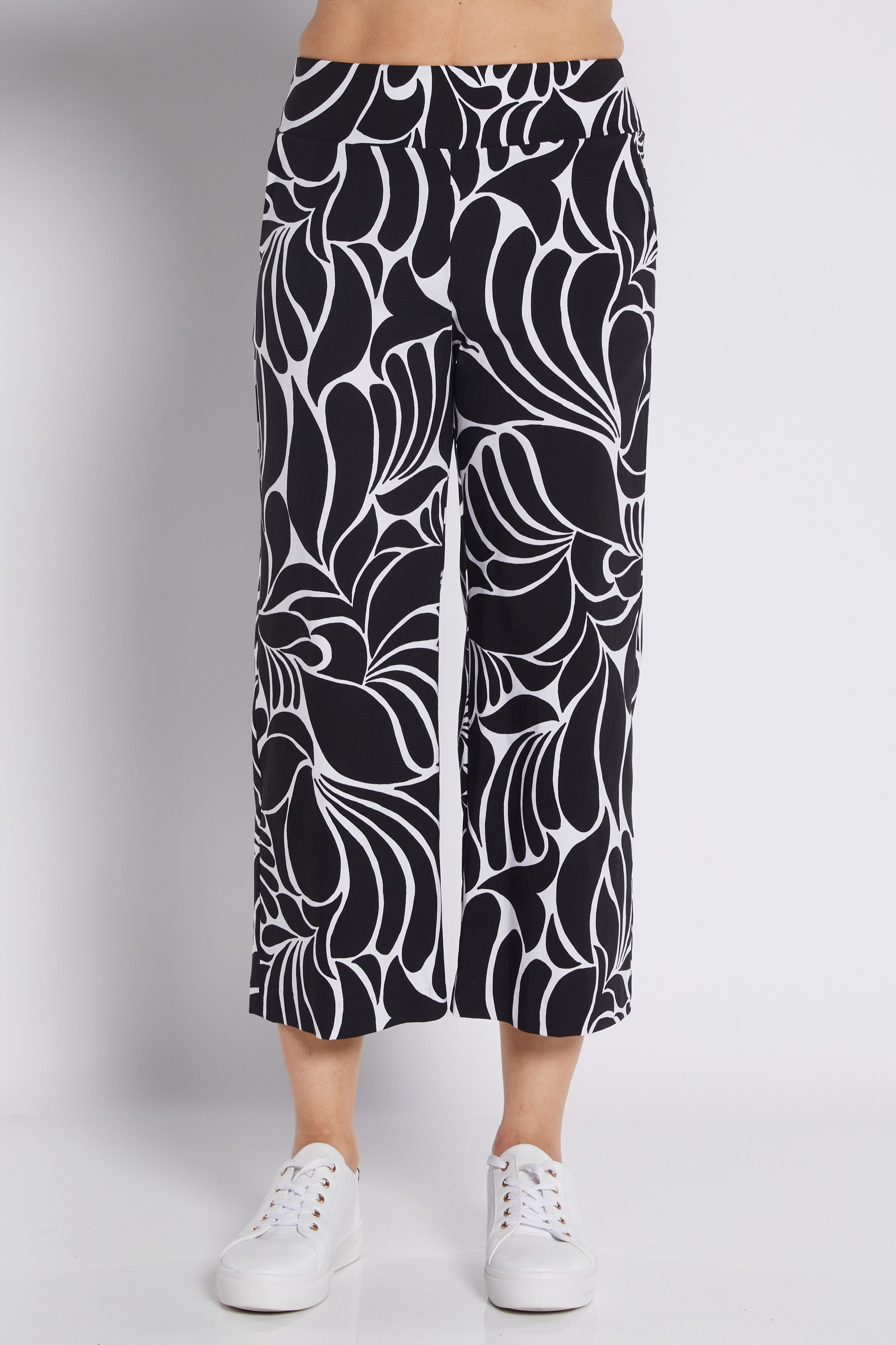 Black and white abstract floral print cropped pants worn by a model with white sneakers, photographed against a light gray studio background.