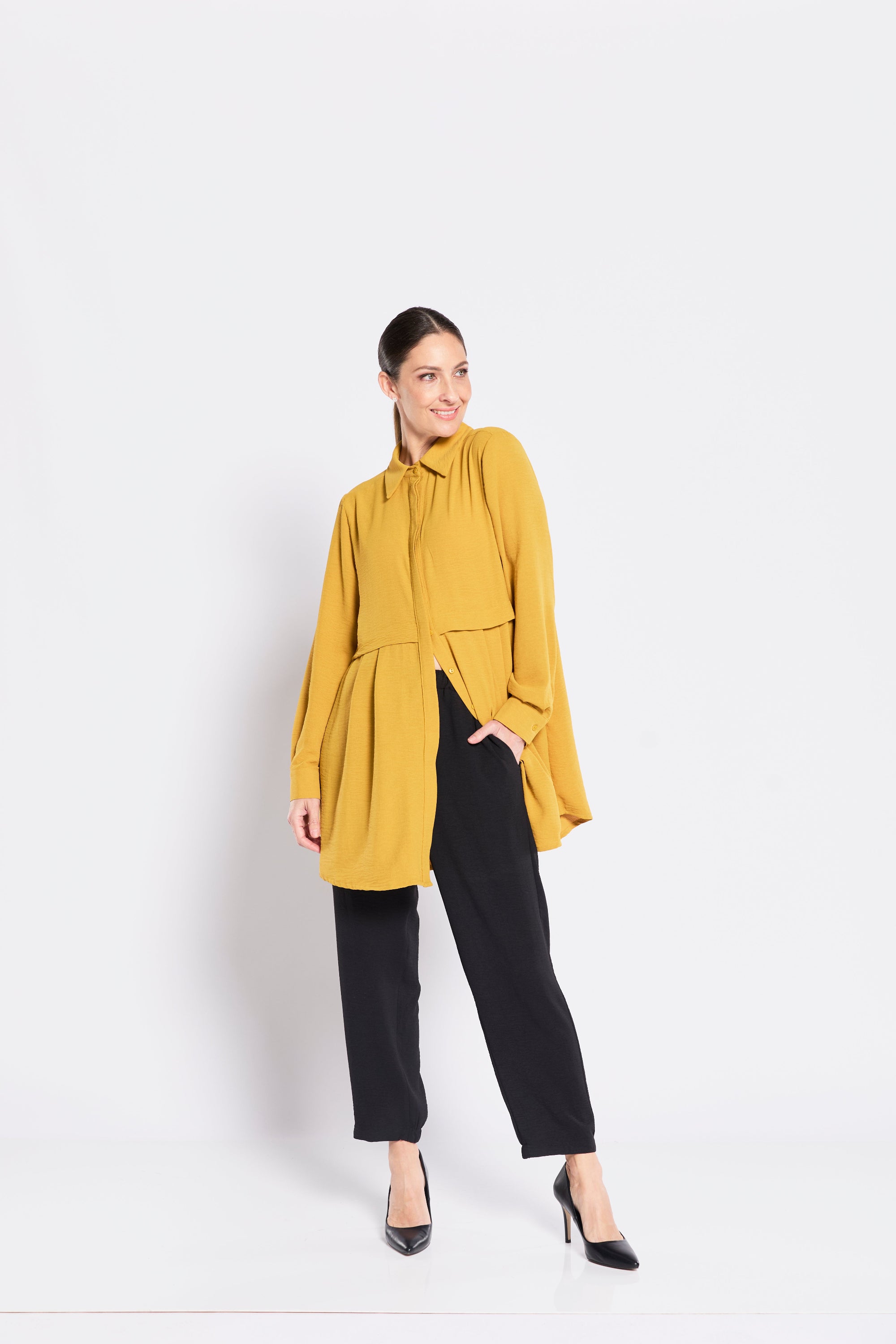 Woman wearing a mustard yellow top and black pants on a white background