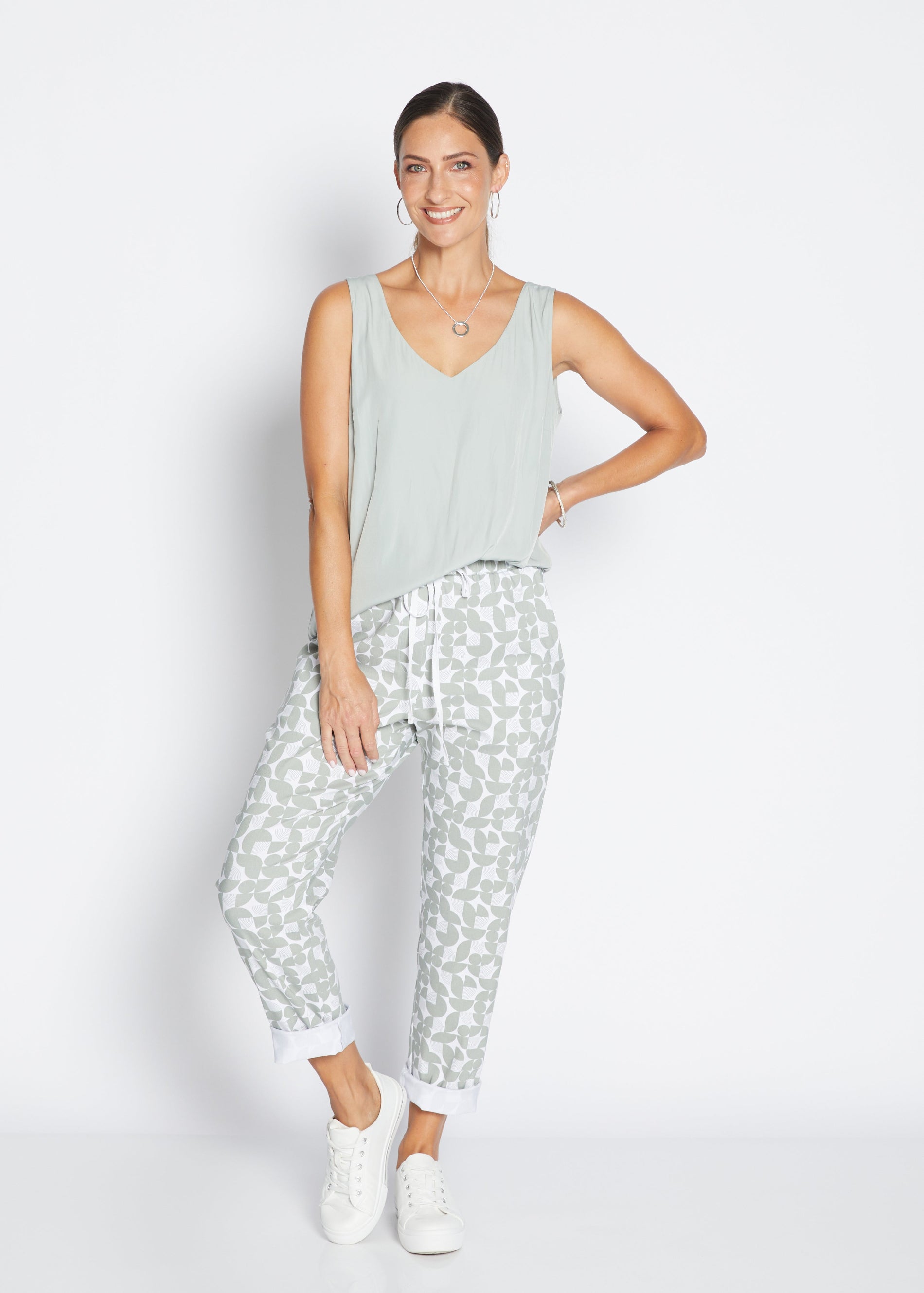 Woman wearing a light green sleeveless top and patterned pants on a white background
