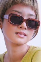 Person wearing tortoiseshell sunglasses with a plain background