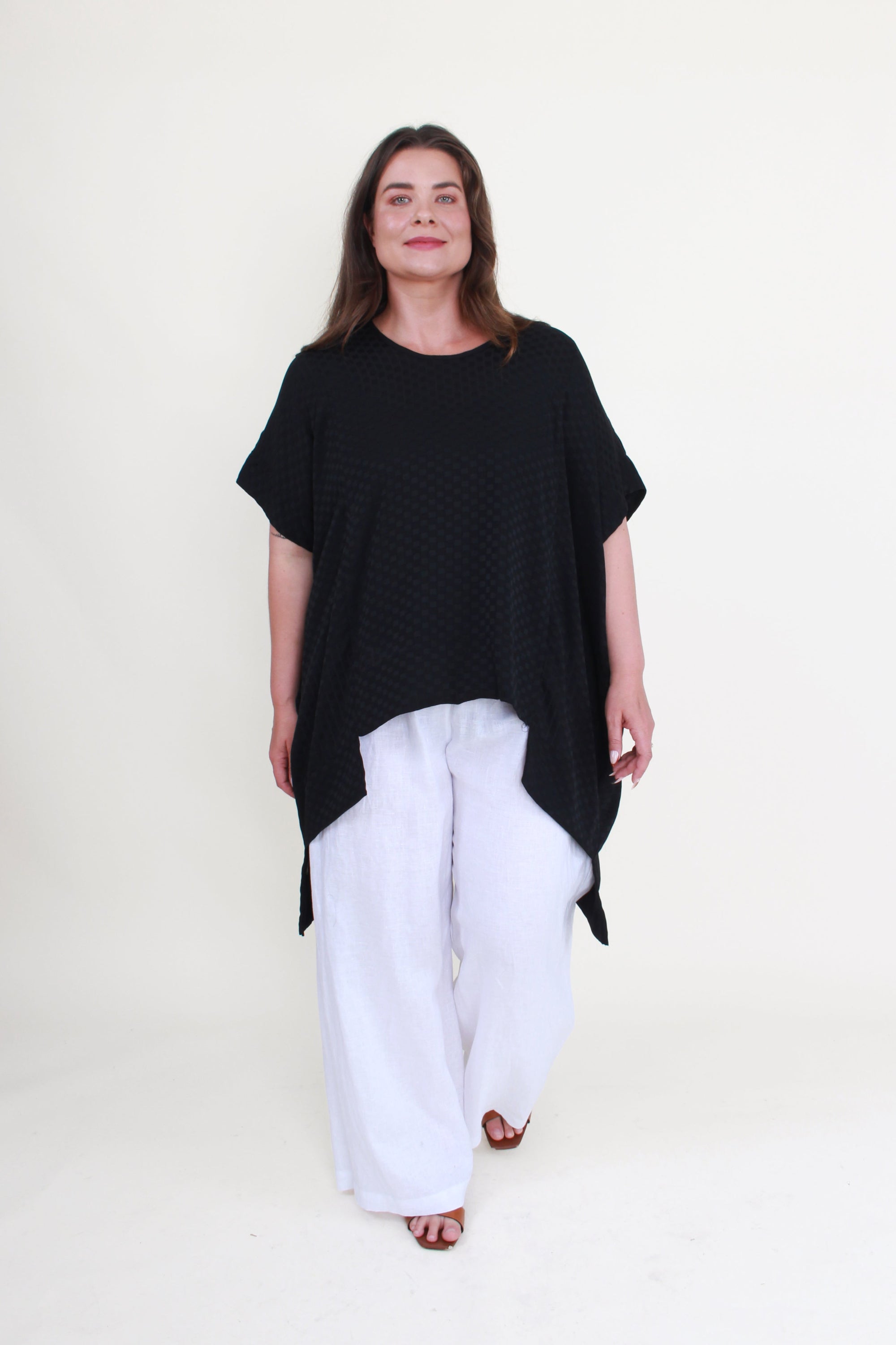 Woman wearing a black oversized top and white pants on a white background
