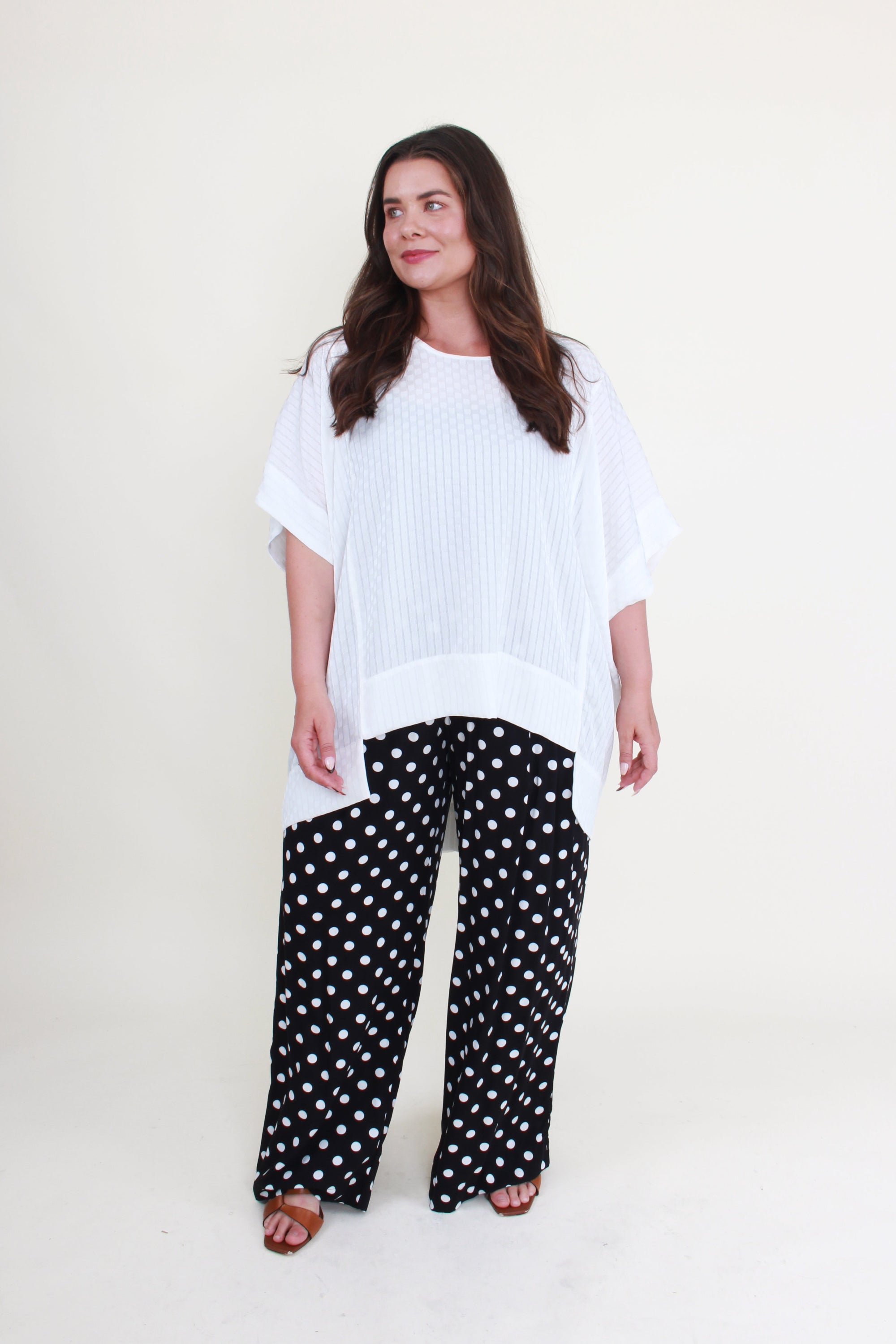 Woman wearing a white oversized top and black polka dot pants on a white background