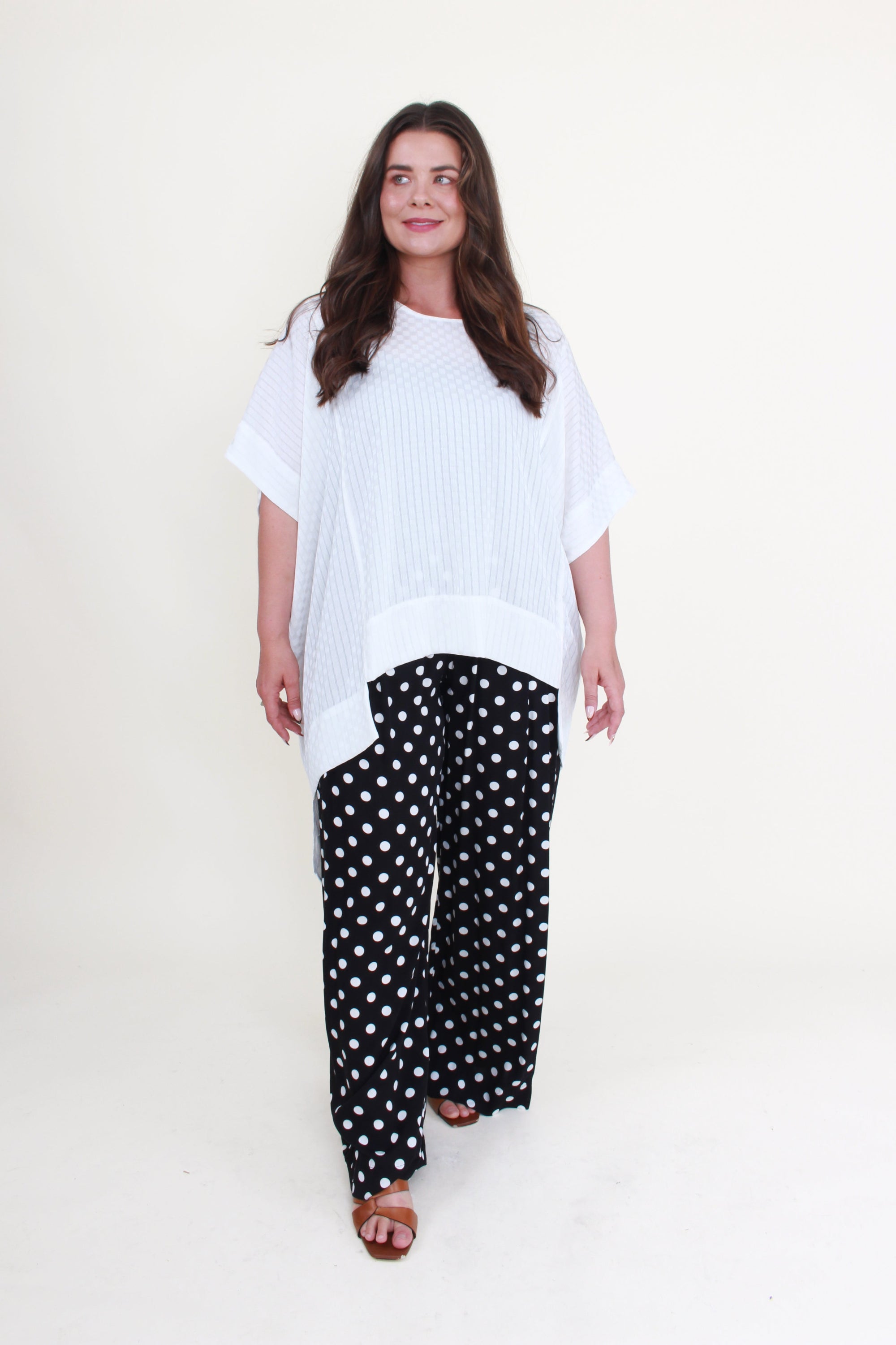 Woman wearing a white top and black polka dot pants on a white background