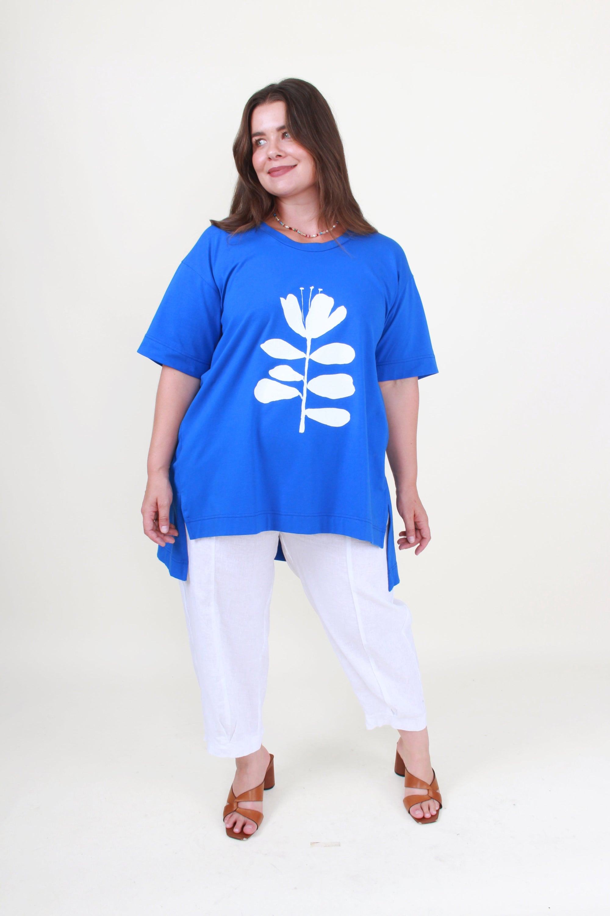Woman wearing a blue tunic with a white floral design on a plain background